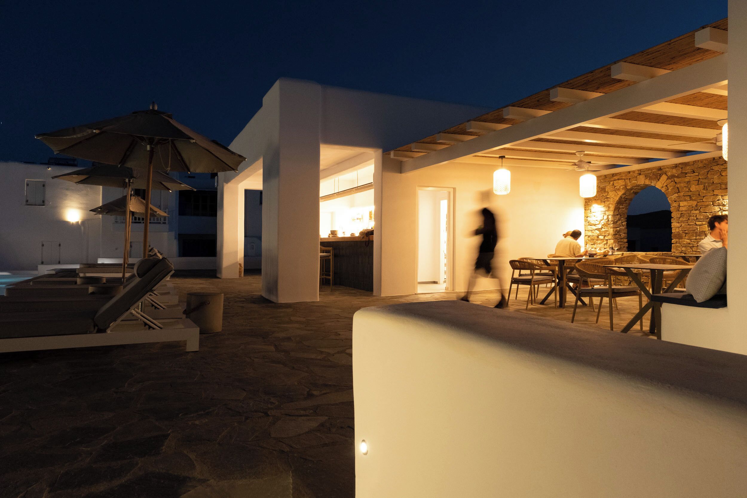 Un espace extérieur aménagé en terrasse, avec une piscine, des parasols et un sol en pierre.