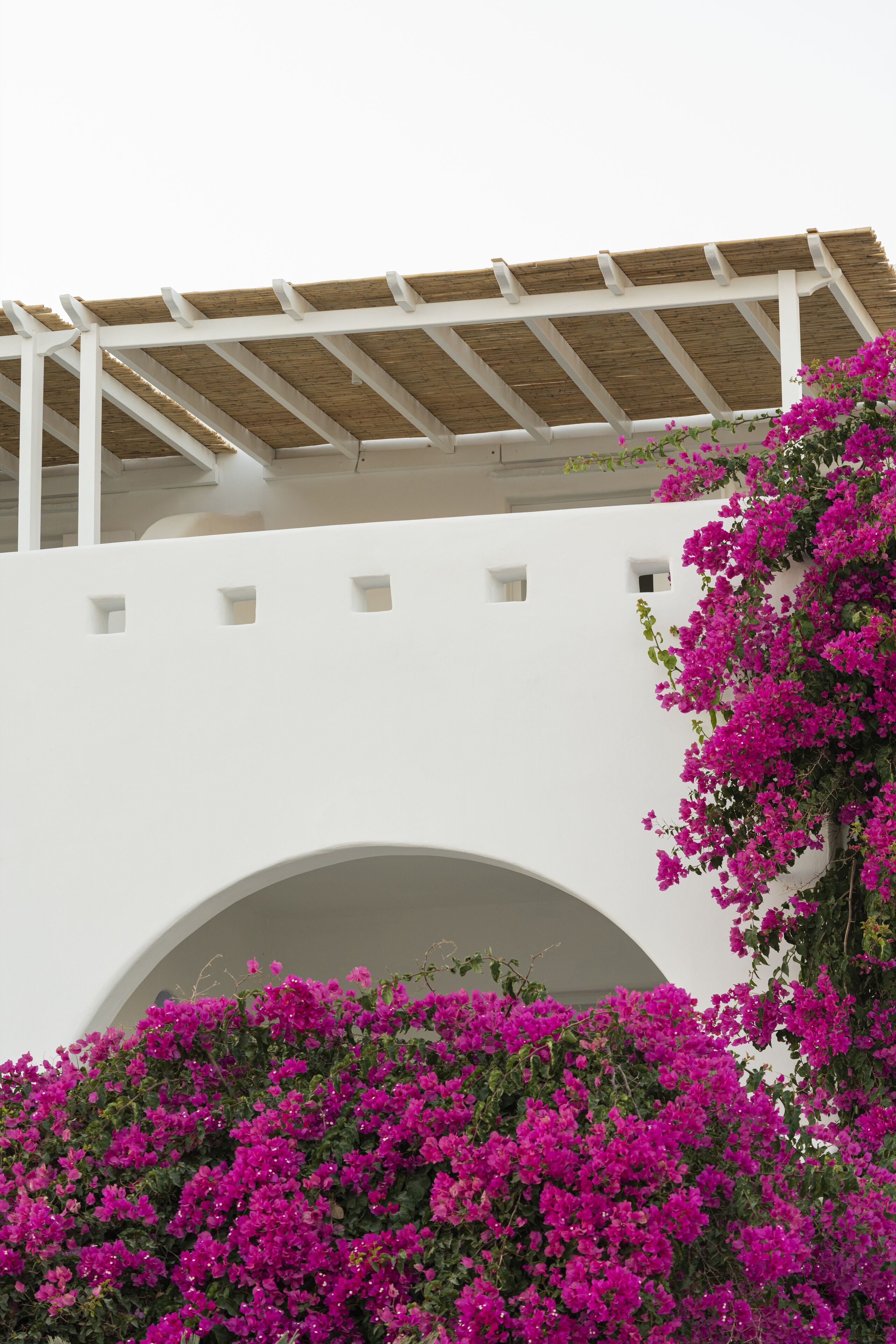 A white building with a wooden pergola and a large archway.