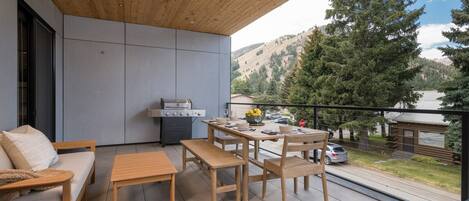 Un patio exterior moderno con techo de madera, una mesa de comedor con sillas, un sofá y una parrilla.