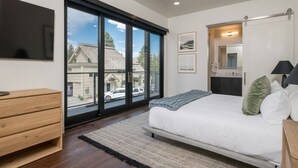 A bedroom with a large sliding glass door to the outside, a bed with white bedding, a wooden dresser, and a flat-screen TV mounted on the wall. - Luxury Condo 5 Blocks from Downtown (Ketchum)