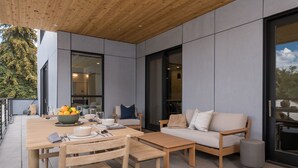 A modern outdoor patio with a wooden table set for dining, a sofa, and a trash bin. - Luxury Condo 5 Blocks from Downtown (Ketchum)
