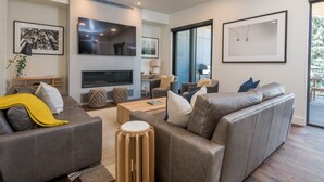 A modern living room with a grey sofa, a coffee table, and a TV. There are framed pictures on the walls and a large window. - Luxury Condo 5 Blocks from Downtown (Ketchum)