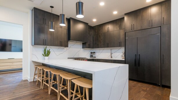 A modern kitchen with dark cabinets, a marble island with bar stools, and pendant lighting. - Luxury Condo 5 Blocks from Downtown (Ketchum)