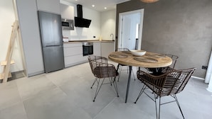 A modern kitchen with a round dining table, wicker chairs, and a hanging light fixture. - Apartamentos Las Indianas (Llanes)