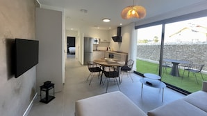 A modern living room with a flat-screen TV mounted on the wall, a dining area with a table and chairs, and a kitchen with a microwave and refrigerator. - Apartamentos Las Indianas (Llanes)