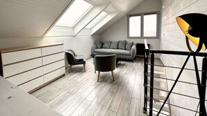 A loft-style room with a sloped ceiling, a grey sofa, a black chair, and a piano. - Duplex, 45 m2, sleeps 8 - Duplex 45 m2, 8 couchages, vue imprenable (Alpe d'Huez)