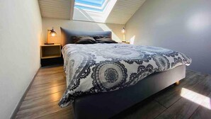 A bedroom with a skylight, a bed with patterned bedding, two bedside lamps, and wooden flooring. - Duplex, 45 m2, sleeps 8 - Duplex 45 m2, 8 couchages, vue imprenable (Alpe d'Huez)