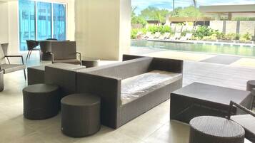 A modern outdoor lounge area with wicker furniture, a pool, and a view of greenery.
