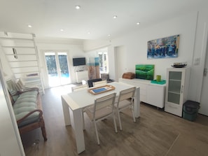 Une cuisine moderne avec des meubles blancs, une table à manger et des chaises. Un téléviseur est fixé au mur et un tableau est accroché au-dessus des meubles.