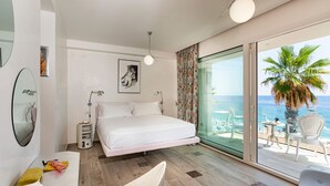 A bedroom with a bed, bedside tables, a mirror, and a view of the beach through large windows.