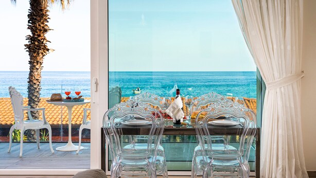 A dining area with a glass table and chairs, a view of the sea, and a palm tree. - Exceptional modern apartment with majestic sea view in Letojanni - DiCasaInSicilia (Letojanni)