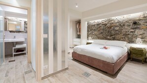 A bedroom with a stone wall, a bed, a nightstand, and a bathroom with a sink and mirror. - Exceptional modern apartment with majestic sea view in Letojanni - DiCasaInSicilia (Letojanni)