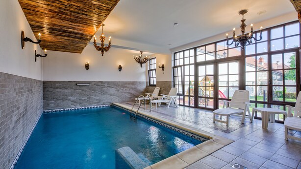 An indoor swimming pool with a wooden ceiling, a chandelier, and a view of the outside through large windows. - Luxury Chalet with private swimmingpool located in residential Saxon area (Cristian)