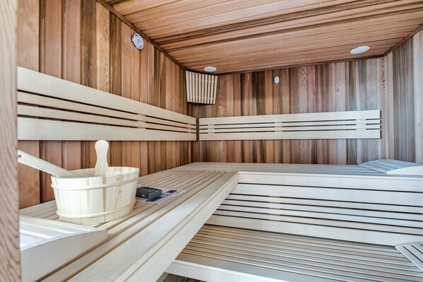 Un sauna avec des parois en lattes de bois, un seau en bois et une horloge au mur.