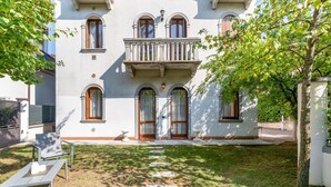 A two-story building with a balcony, a paved entrance, and a grassy yard with a pathway. - GuestHost - Bright and welcoming 70sqm apartment with garden equipped with table and chairs, located on the ground floor of a period building that can accommodate up to 5 people! The apartment is located a few steps from the center of Vicenza. Convenient (Vicenza)