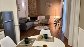 A modern living room with a fireplace, a dining area with a round table, and a kitchen area with a refrigerator. - GuestHost - Bright and welcoming 70sqm apartment with garden equipped with table and chairs, located on the ground floor of a period building that can accommodate up to 5 people! The apartment is located a few steps from the center of Vicenza. Convenient (Vicenza)