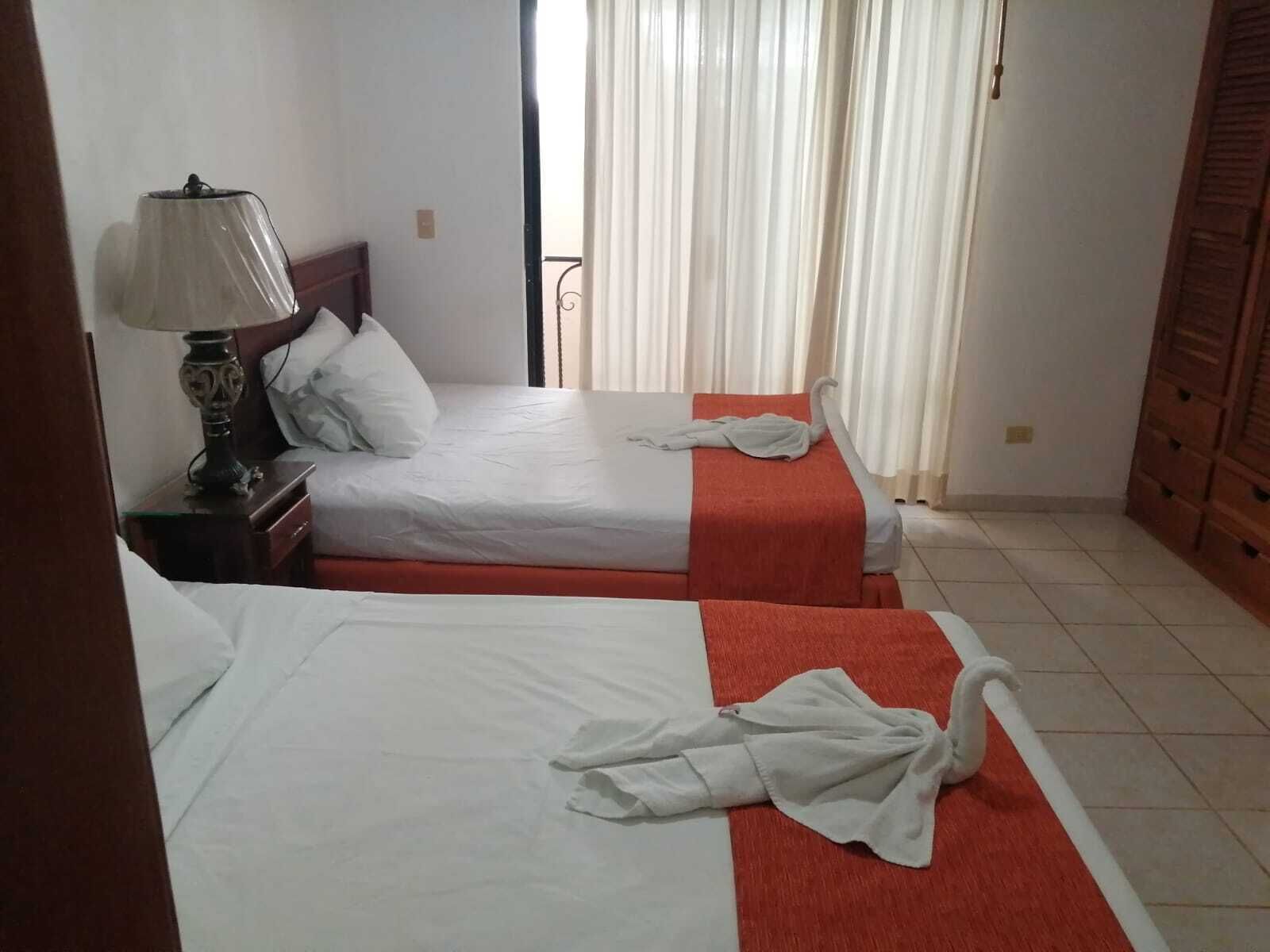 A hotel room with two beds, a nightstand with a lamp, and a wardrobe.