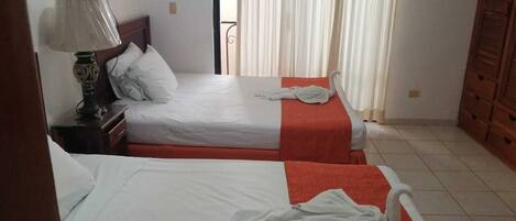 A hotel room with two beds, a nightstand with a lamp, and a wardrobe.