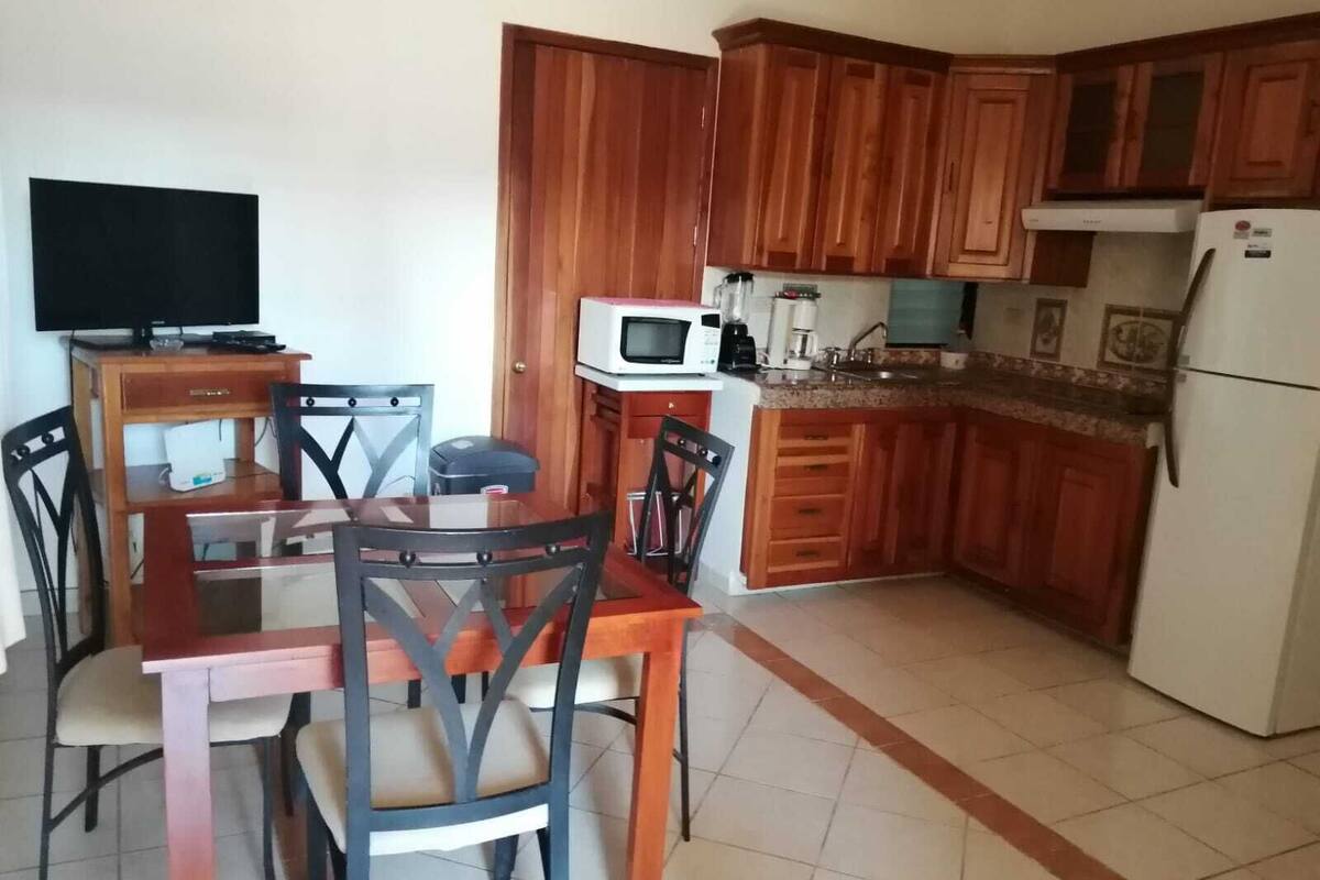 A compact kitchen with wooden cabinets, a microwave, a refrigerator, and a dining table with chairs.