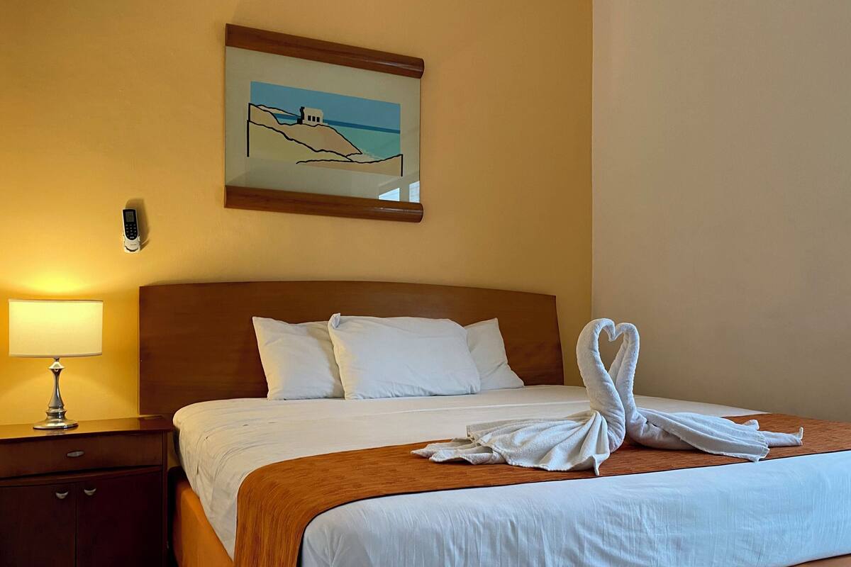 A hotel room with a bed, a nightstand, a lamp, and a painting on the wall.