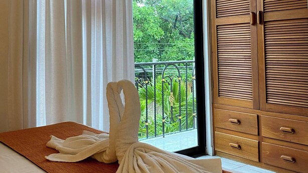 A hotel room with a bed, a wooden wardrobe, and a view of greenery through a window. - Quinta Sea (Playa del Carmen)