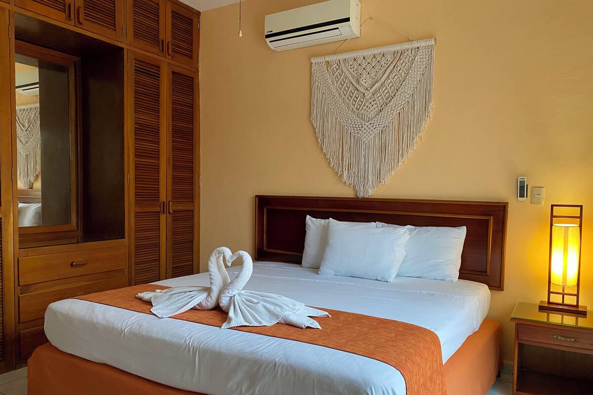 A hotel room with a large bed, wooden wardrobe, and a wall-mounted air conditioner.