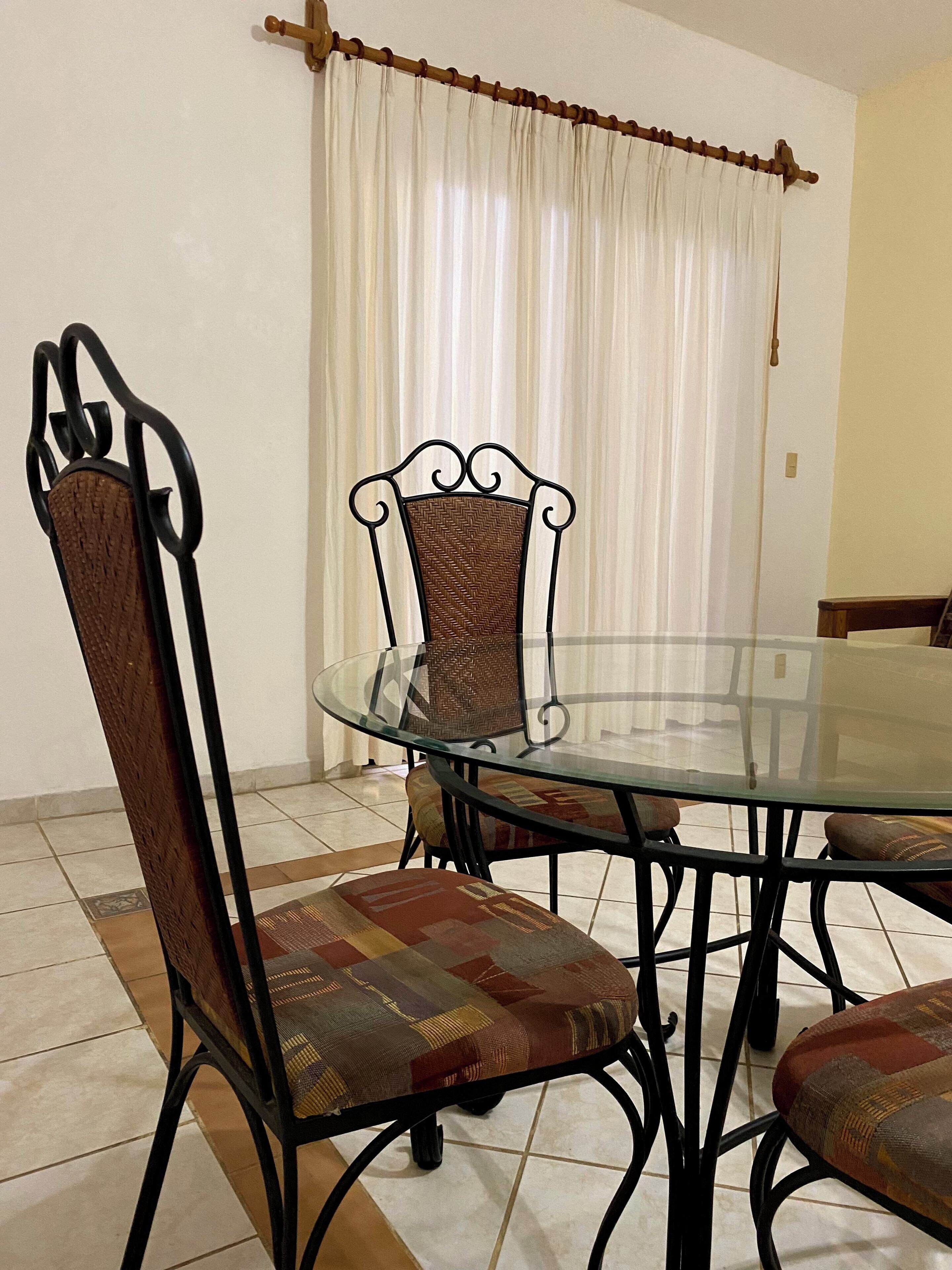 A dining area with a glass table surrounded by metal chairs with cushioned seats.