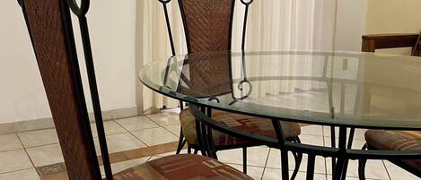 Un comedor con una mesa de vidrio rodeada de sillas de metal con asientos acolchados.