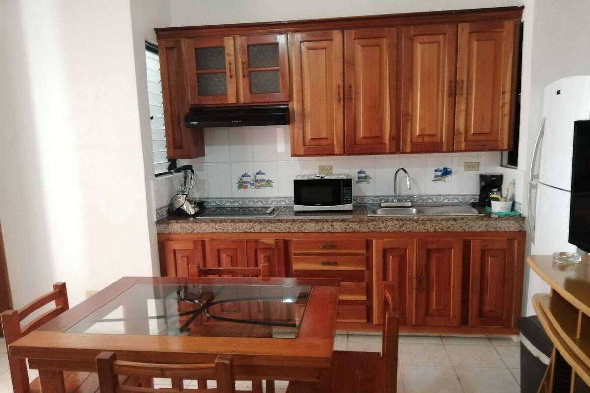 A kitchen with wooden cabinets, a microwave, a sink, and a dining table with chairs.
