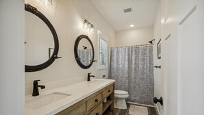 A bathroom with a double sink vanity, a toilet, a shower curtain, and a large mirror. - Your Fresh Beach Oasis! (Corolla)