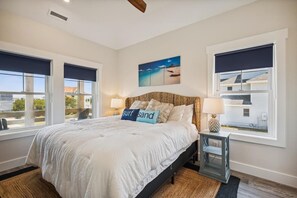 A bedroom with a large bed, two bedside tables, a nightstand, a painting on the wall, and a view through the window.