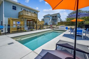 A swimming pool with a wooden deck, lounge chairs, and umbrellas.