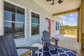 A covered porch with two Adirondack chairs, a wooden deck, and a view of the surrounding landscape.