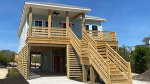 A two-story building with a wooden deck and stairs leading to a balcony. - Your Fresh Beach Oasis! (Corolla)