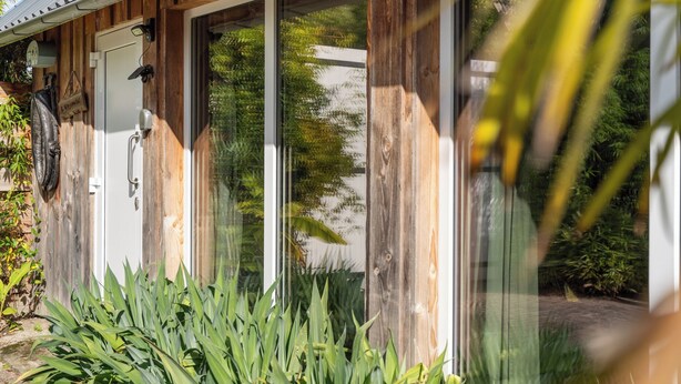 Ein Holzgebäude mit großen Glasüren, einer weißen Tür und einem kleinen Vorbereich mit Pflanzen.