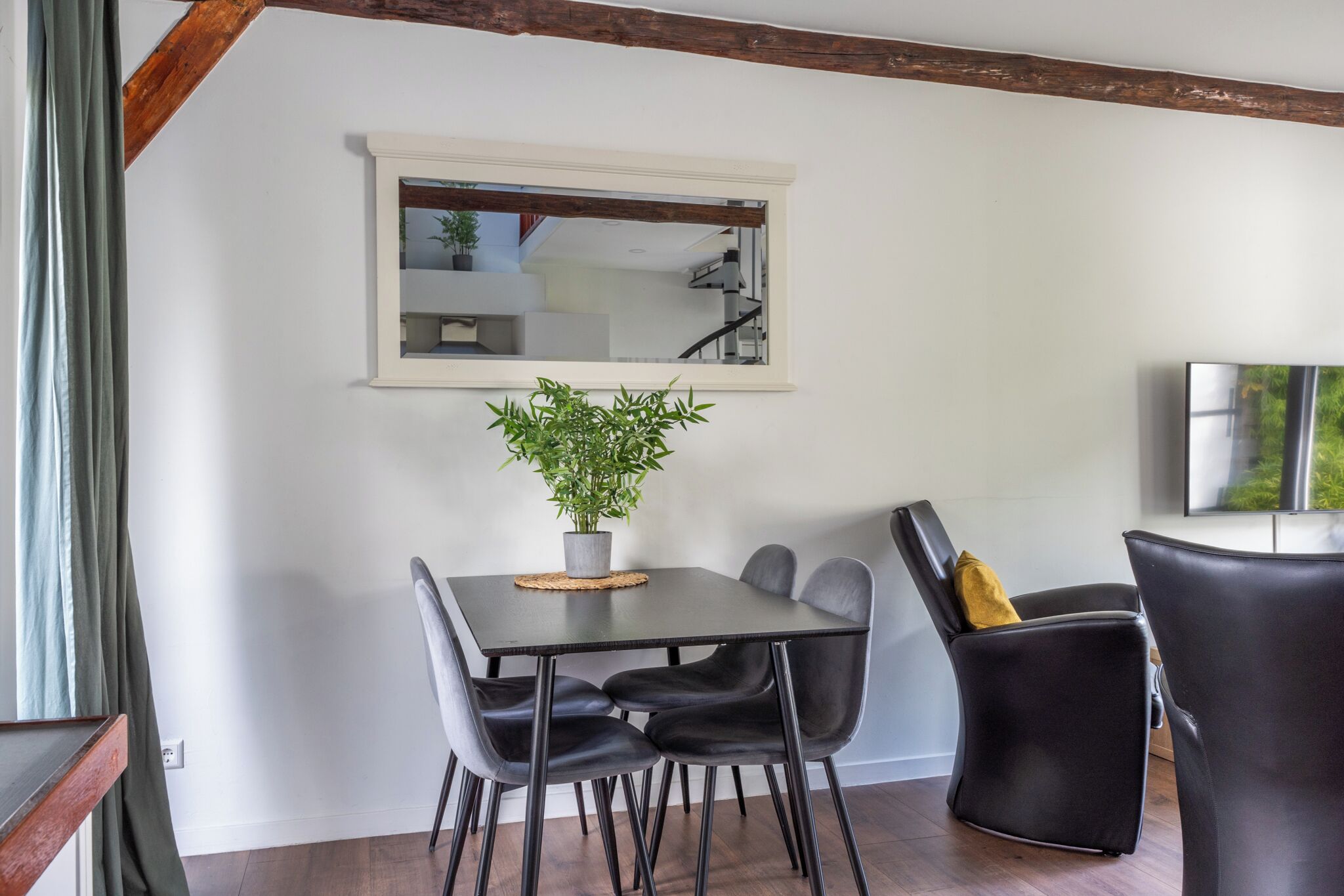 Ein Essbereich mit Tisch, Stühlen, einer Topfpflanze und einem Spiegel an der Wand.