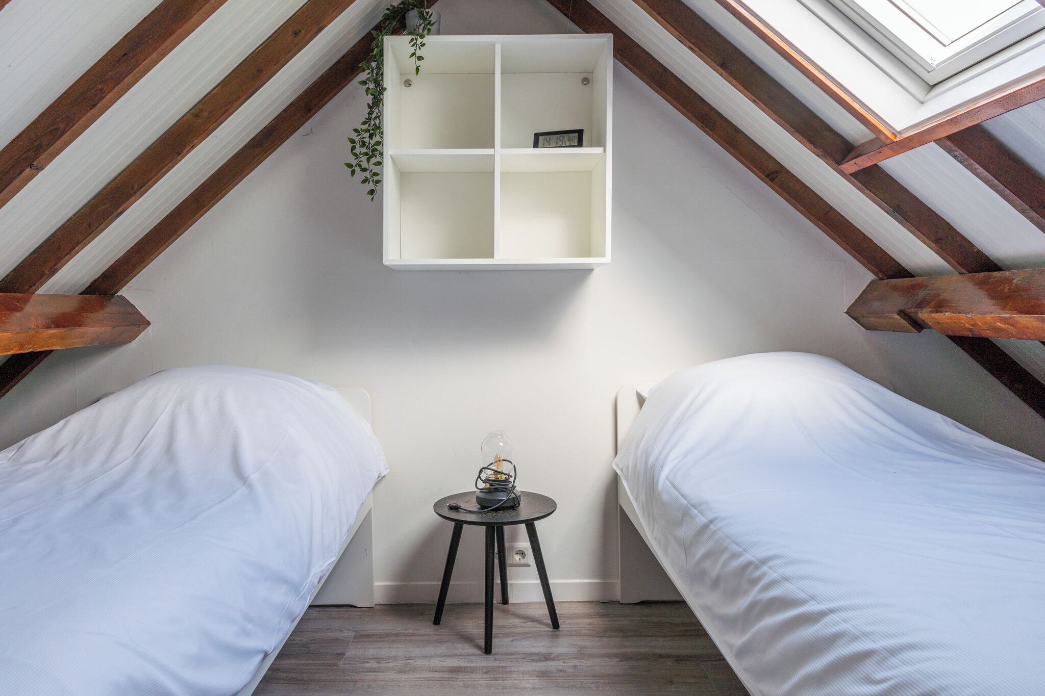 Un dormitorio acogedor en el ático con dos camas, una mesita pequeña y un estante blanco.