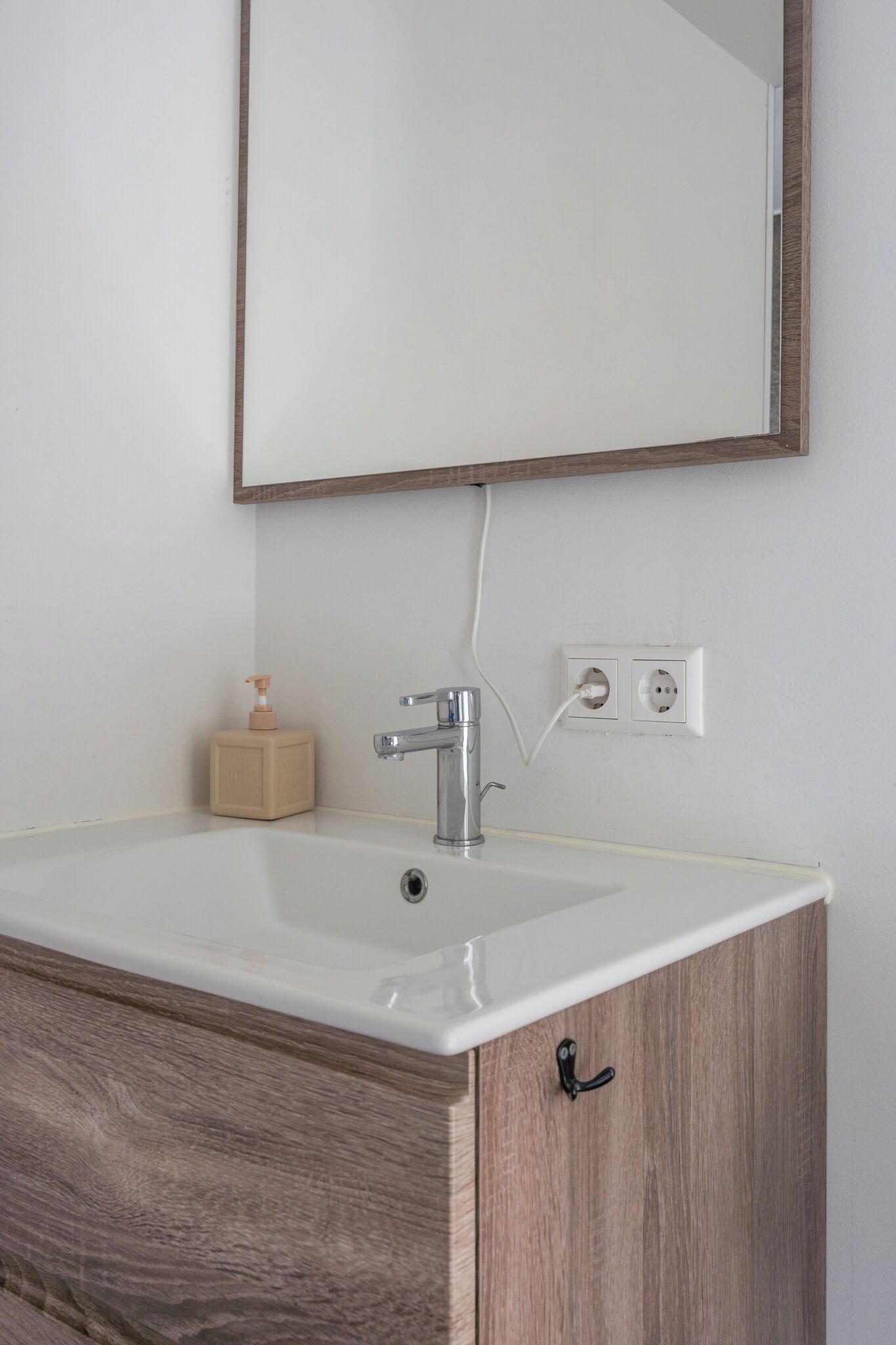 Un baño con lavamanos blanco, armario de madera y un espejo encima.