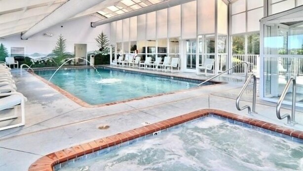 Ein Hallenbad mit Whirlpool, Liegestühlen und einem durch eine Glasscheibe abgetrennten Bereich.