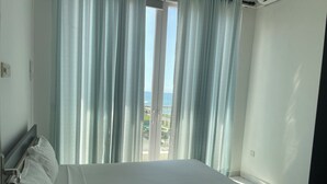 A hotel room with a bed, a window with curtains, and a view of the sea.