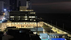 A multi-story hotel with a swimming pool, located near a beach with high-rise buildings in the background.