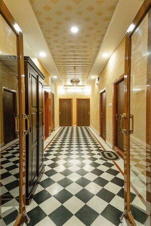 Un couloir doté d’un sol à carreaux, de portes en bois et d’un plafond orné de motifs.