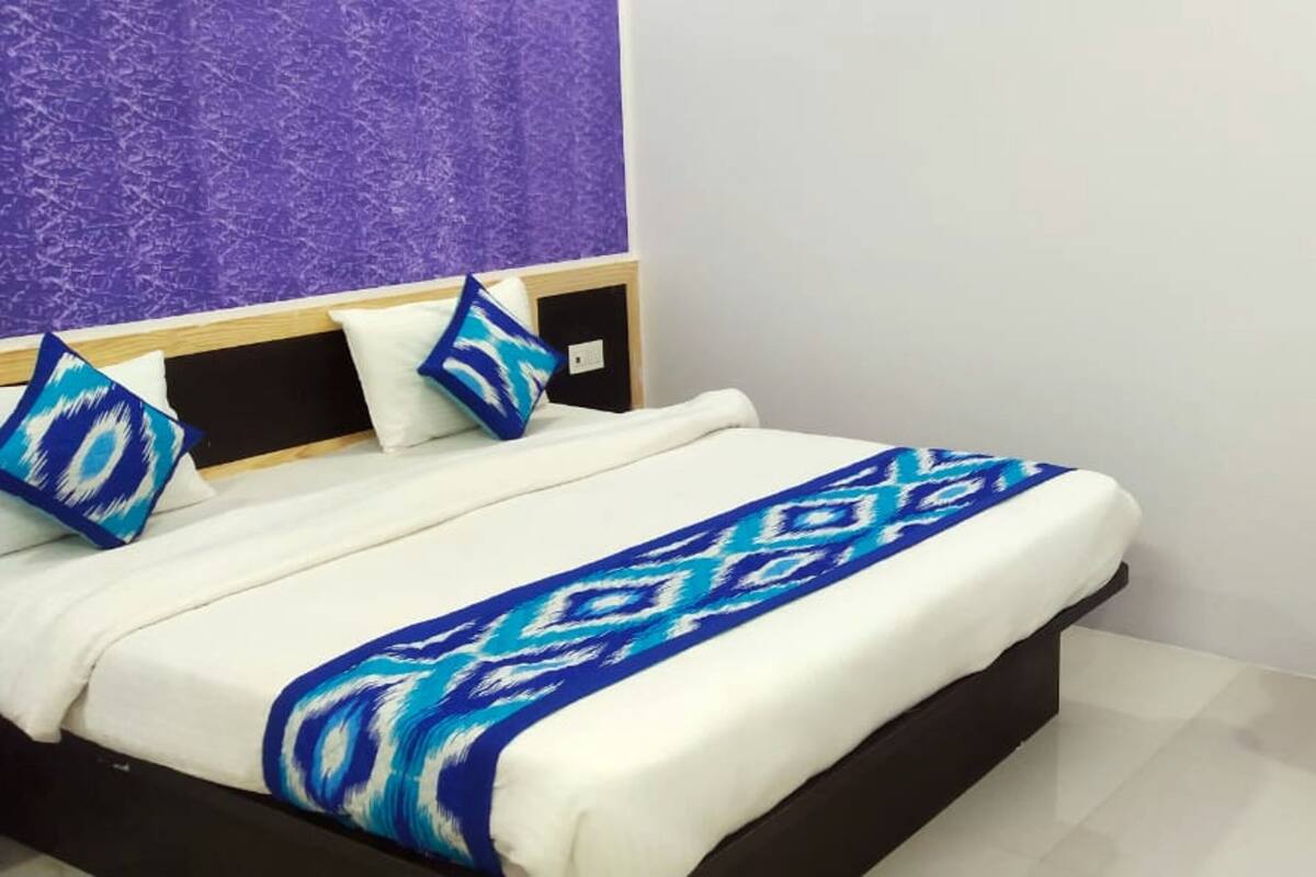 Ein Bett mit einem gemusterten Überwurf, ein lila Sessel und eine Wand mit strukturierter Musterung.