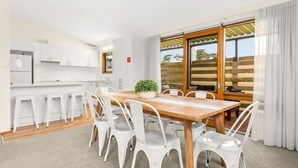 A modern kitchen with white cabinets, a wooden dining table with white chairs, and a large window with a view of trees. - Views on Broadway - Pet friendly 4 bedroom home (San Remo)