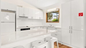 A modern kitchen with white cabinetry, a built-in dishwasher, and a window with a view of greenery. - Views on Broadway - Pet friendly 4 bedroom home (San Remo)