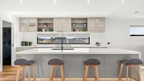 A modern kitchen with a large island, bar stools, and built-in shelves with various items. - The Manor with spa in Cowes (Cowes)