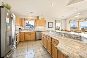 A modern kitchen with wooden cabinets, a stainless steel refrigerator, and a large window offering a view of the ocean.