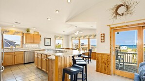 A kitchen with wooden cabinets, a large island, and a view of the ocean through the windows. - 6151 Once Upon a Tide * Almost Oceanfront (Nags Head)