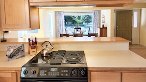A kitchen with wooden cabinets, a stove, and a view of an outdoor dining area. - Fisherman's Delight in Waldport! Dog Friendly! Hot tub! (Waldport)