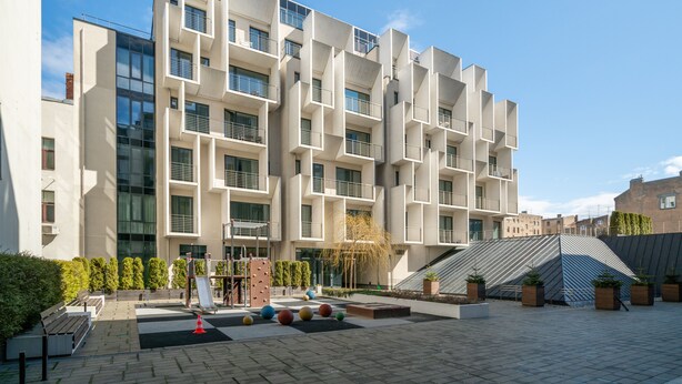A modern building with a geometric facade, multiple balconies, and a courtyard with seating and decorative elements. - Easyrooms Dzirnavu (Riga)
